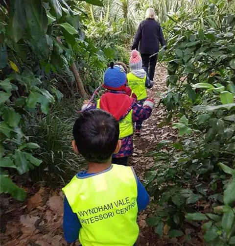Children in high-visibility vests walking a bush track during Bush Kinder