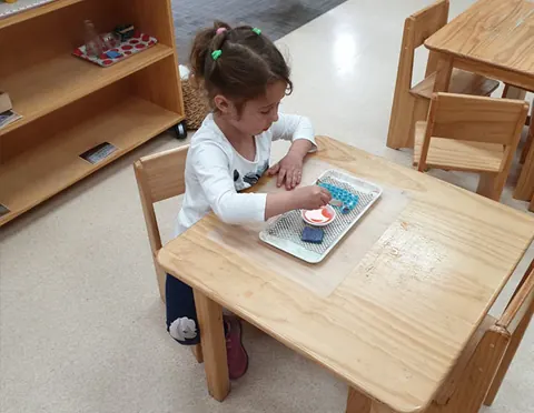 Child concentrating on a practical life activity at a classroom table