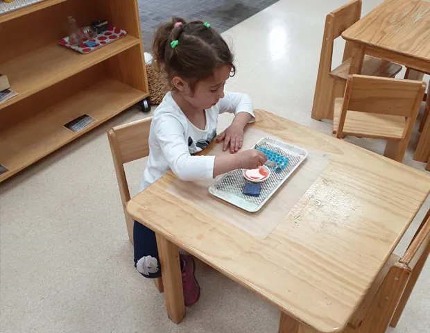 Child concentrating on a practical life activity at a classroom table