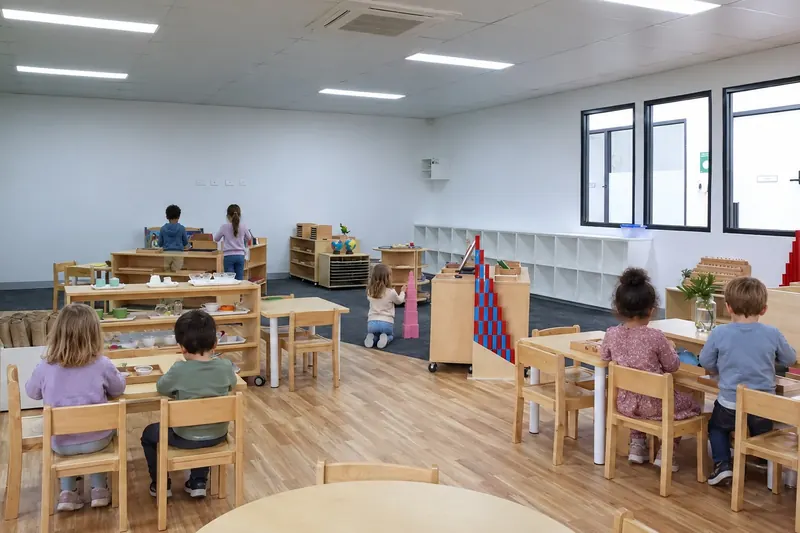 Kindergarten children working at child-sized tables and Montessori shelves in our classroom