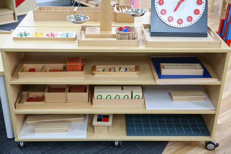 Maths shelf with number rods, sandpaper numerals, a clock and counting materials