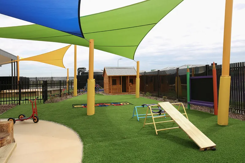 Landscaped playground with shade sails, a timber cubby house and climbing frame