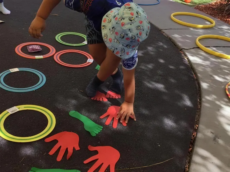 Child playing a hands-and-feet coordination game with coloured hoops